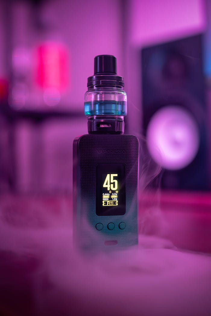 contact-img Close-up of an electronic vape device with illuminated screen and surrounding vapor, set against a purple-lit background.