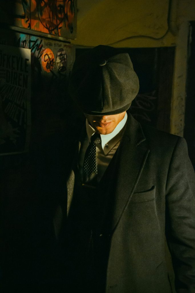 pexels photo 22481696 22481696 Stylish man in retro attire with hat, captured in a shadowy, artistic ambiance.